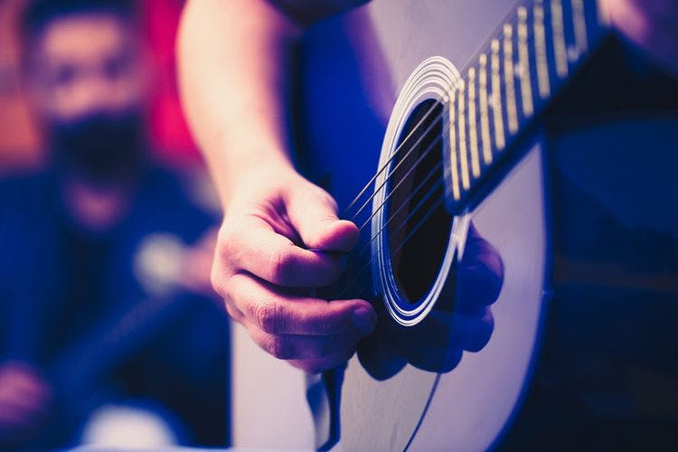 Close up of a person finger strumming a purple acoustic guitar