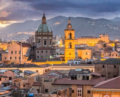 Palermo city skyline, with a large domed church and tower and with mountains in the distance