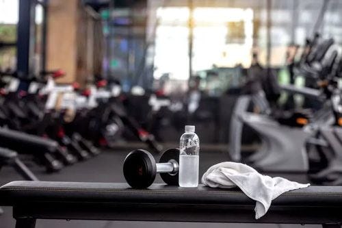 A dumbbell, water bottle, and towel on a bench in a gym