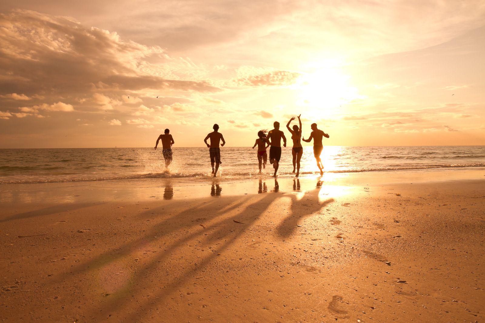 A group of friends staying in our spring break vacation rentals, silhouetted by the sun running towards the water on a beach