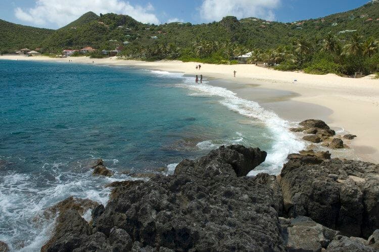 A white sand beach in St Barts with forest-covered mountain in the background