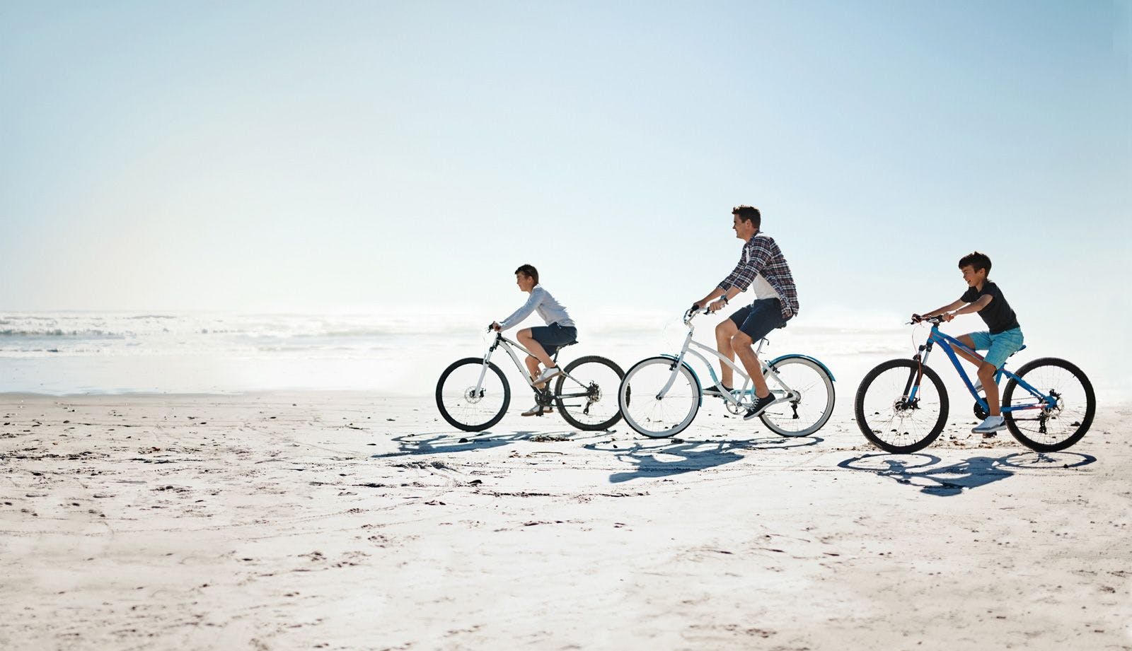 A man and two children riding bicycles along a beach