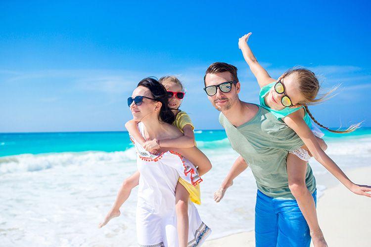 A family with two kids walks along a white sand beach