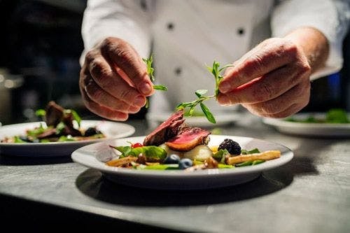 A private chef adding herb garnish to a meat dish