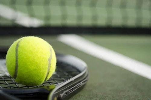 Tennis ball resting on a racket on a tennis court