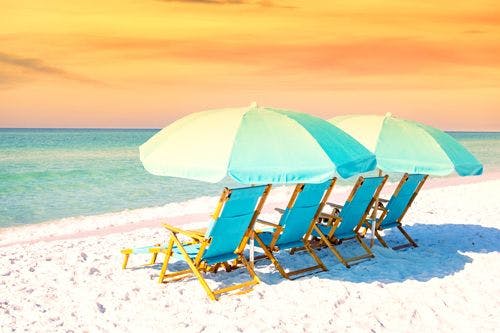 Bright blue beach chairs and umbrellas on a white sand beach at sunset