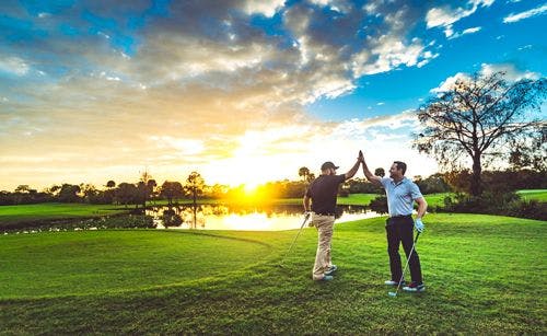 Two golfers high five on a golf course at sunset