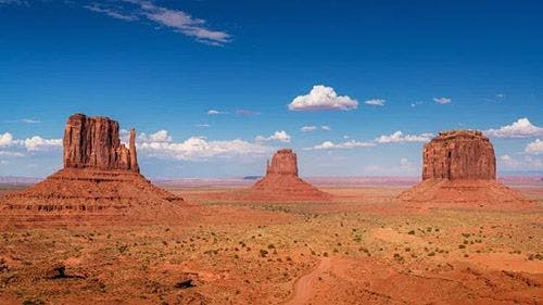 Three large rock formations rising out of the dry ground in Monument Valley