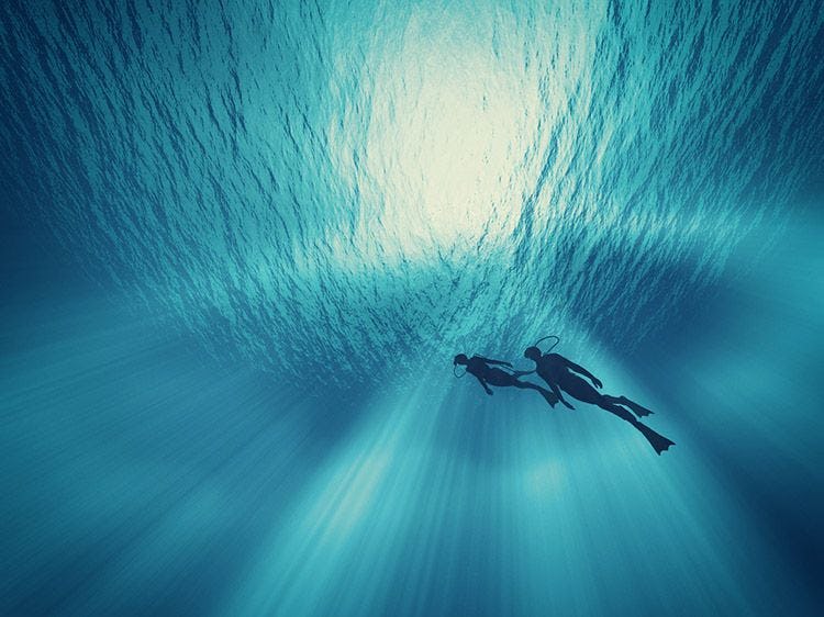 Two divers from below with th sun streaming through the ocean surface above them