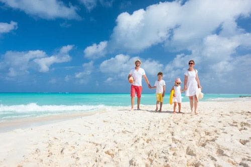 A family of four people walking along a white sand beach