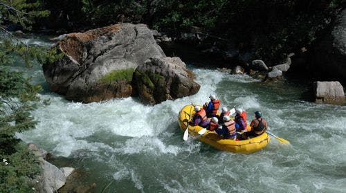 A group of people white water rafting in a yellow boat