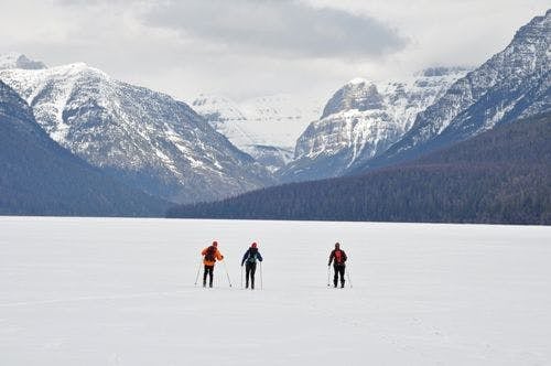 Three people cross-country skiing in a valley surrounded by mountains in Montana