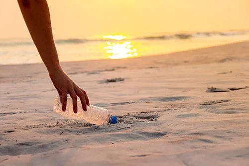 A hand reaching down to pick up a bottle from the sand