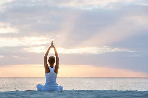 A woman sits on a beach at sunrise doing yoga