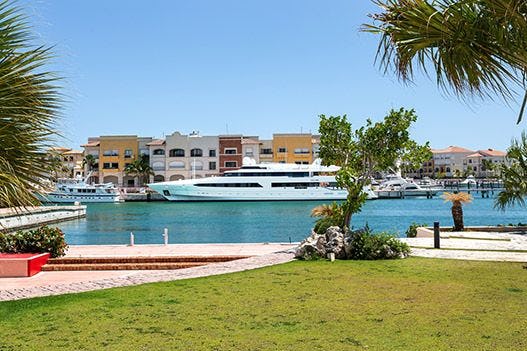 A large white yacht in Cap Cana marina with colorful buildings behind