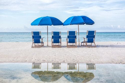 Four blue sun loungers and two blue parasols on a white sand beach facing the sea