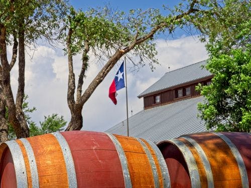 Wine barrels in front of a winery flying the Texas flag