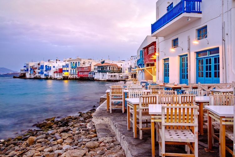 Little Venice in Mykonos with white painted buildings with colorful window shutters against the water of the Aegean Sea