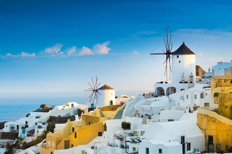 Small windmills and white and yellow cube shaped buildings on a hillside in Santorini