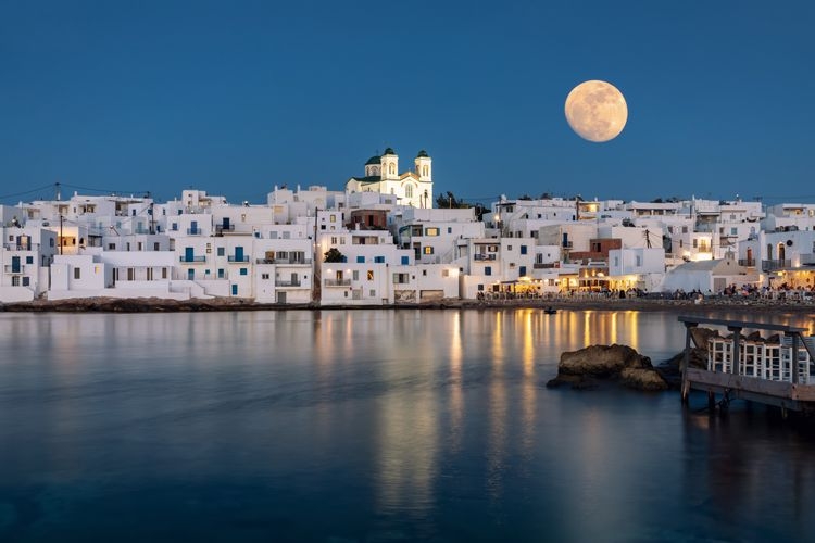 A full moon over the traditional Greek town of Naousa in Paros, with white-painted sugar cube houses by a harbor