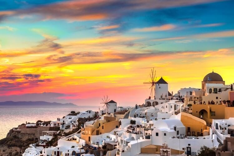A colorful sunset over the town of Oia in Santorini, with white sugar cube houses and windmills