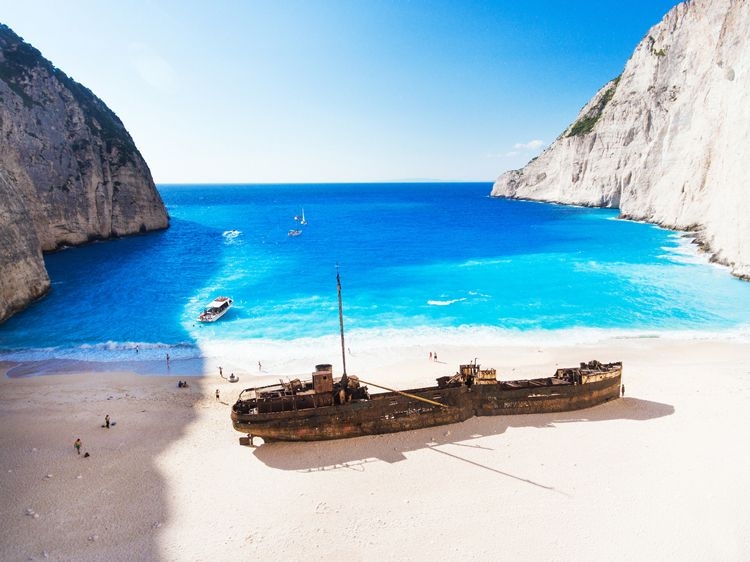 An old shipwreck on a white sand beach in Zante, Greece, with tall white sea cliffs forming a cove around the beach