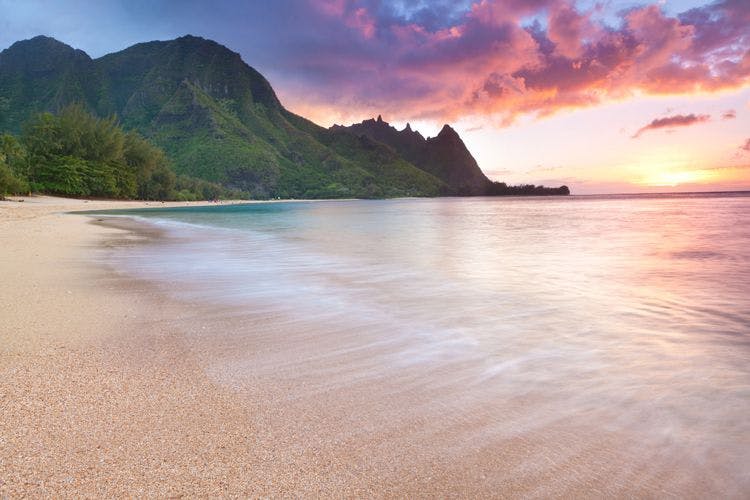 Sunset view of a white sand beach and mountains in Hawaii