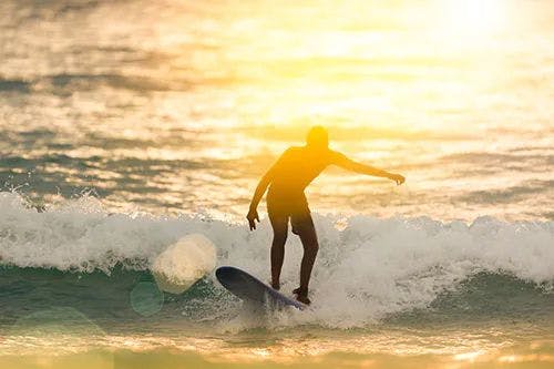 A person surfs a wave at sunset