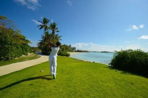 A person dressed in white swings on a golf course