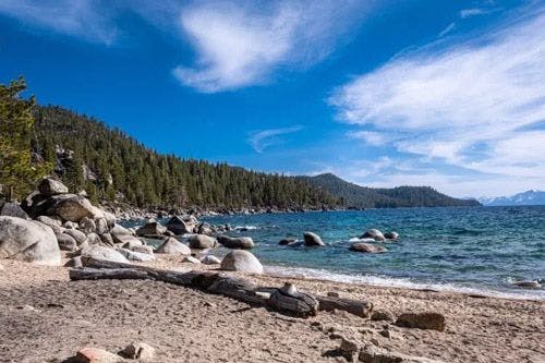 A sandy beach with large rocks and trees lining the shore of Lake Tahoe