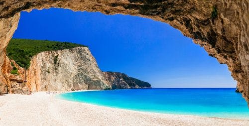 View of a white sand beach in Lefkada through a rock archway