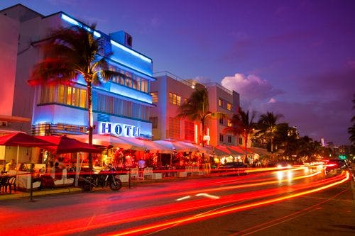 Ocean Drive road in Miami at night with car lights streaking down the road and neon-lit hotels