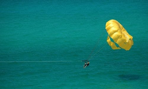 A couple parasailing on a yellow parachute against turquoise sea