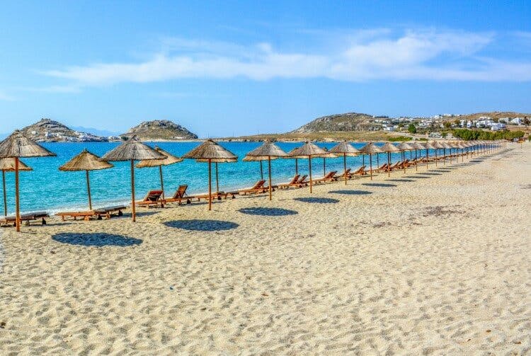 A white sand beach in Mykonos with parasols and sun loungers