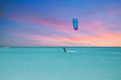 A kite surfer in the Caribbean Sea against a pink and blue sunset sky