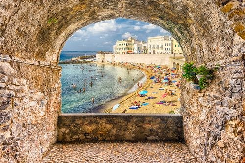 View of beach and seafront buildings through a stone archway in Gallipoli