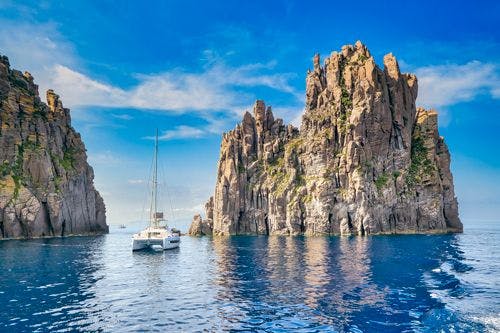 A catamaran by large rock formations in the sea in the Aeolian Islands