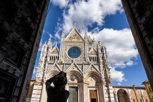 A woman stands taking a photo of Siena cathedral