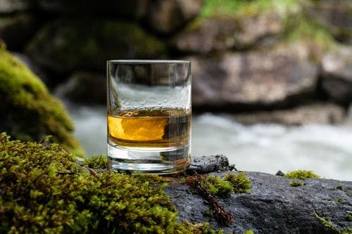 A glass of whiskey on a rock in front of a river