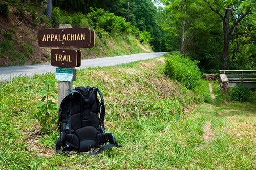 A black backpack resting against a sign reading Appalachian| Trail