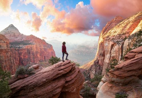 A woman standing on a rock precipice overlooking canyon landscape in Zion National Park