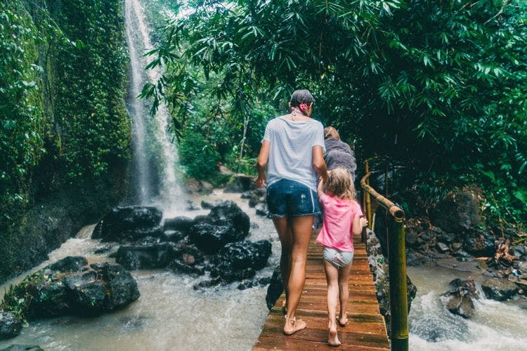 A family crossing a wooden bridge by a waterfall