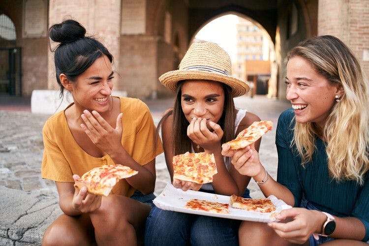 Friends enjoy pizza whilst sitting along along an Italian street
