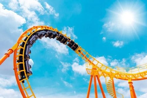 Yellow and orange rollercoaster track with cars on against a blue sky