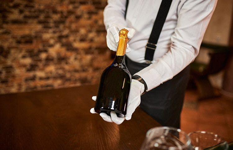 A white-gloved waiter presenting a bottle of champagne