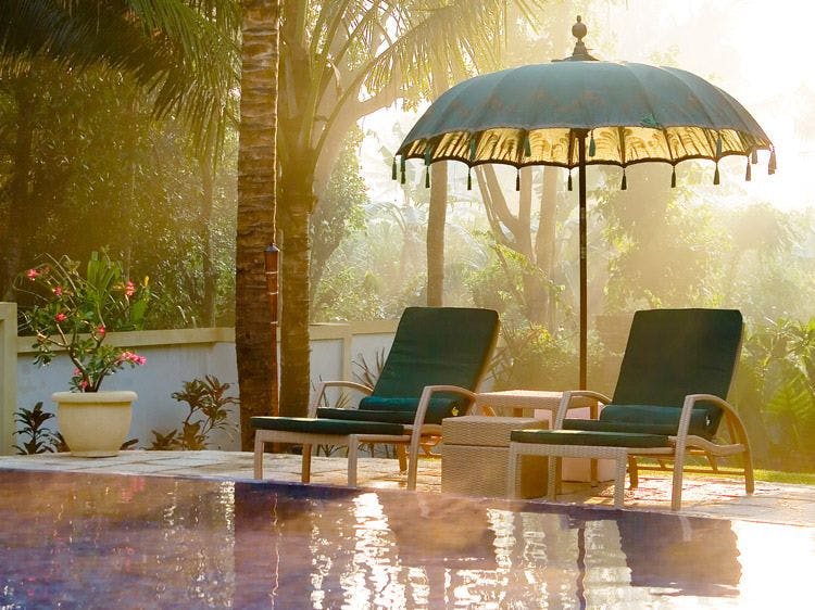 Two sun loungers and a parasol by a pool with palm trees behind