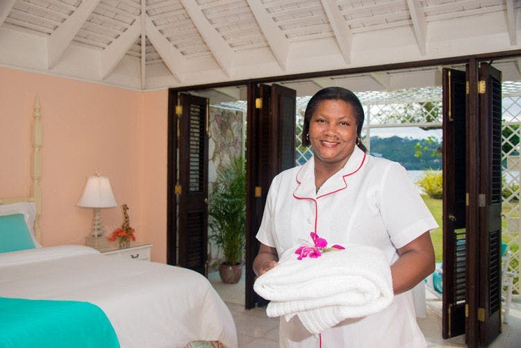 A lady working as a housekeeper in a Caribbean villa with an armful of towels