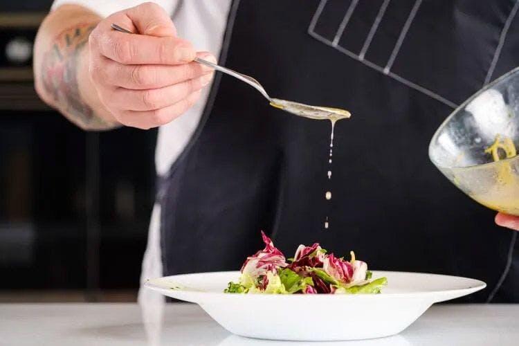 A chef dripping sauce from a spoon onto a salad