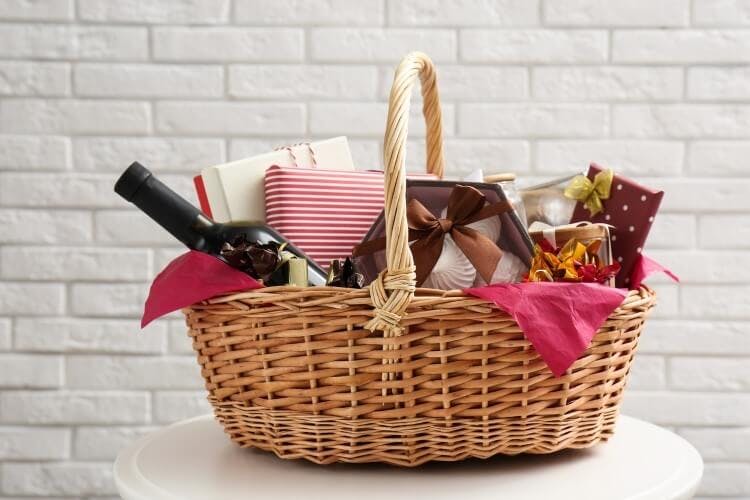 A wicker hamper filled with luxury goods including a bottle of wine, cupcakes, and chocolate
