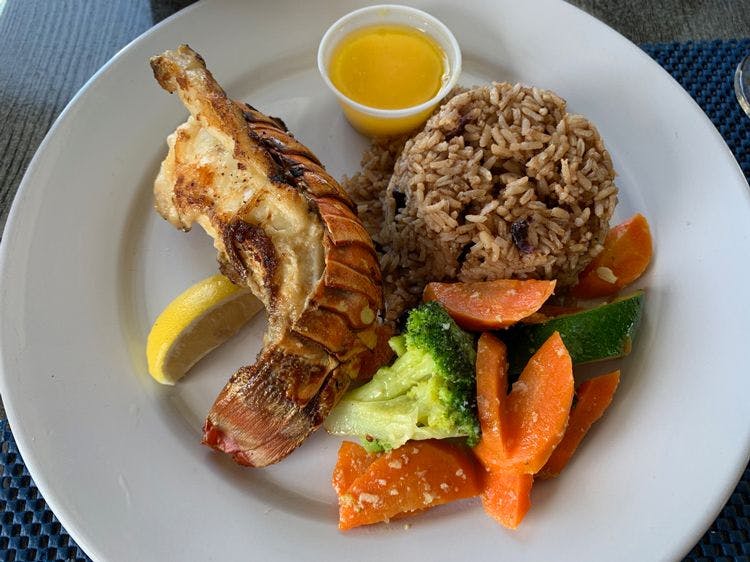 A plate of Caribbean food including lobster tail, beans, and rice